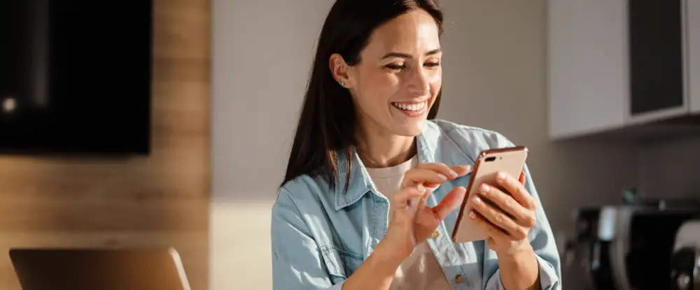 Een breed lachende vrouw kijkt op haar smartphone, ter illustratie van een zeer tevreden klant.