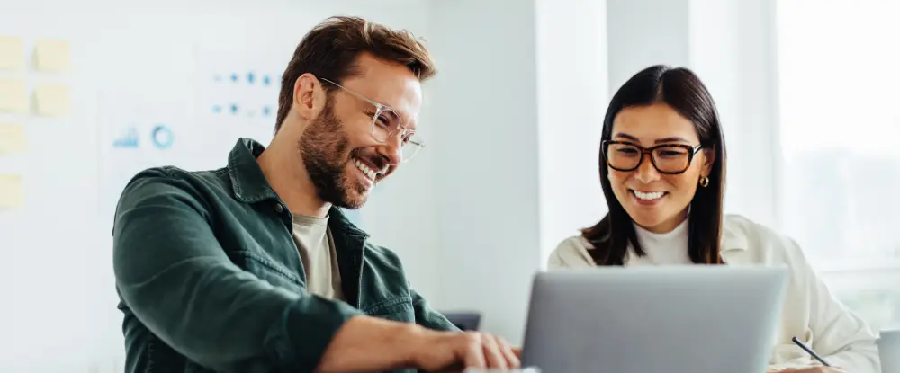 Twee lachende collega's kijken samen naar een CSAT score op een laptop