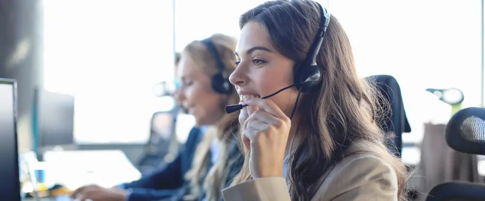 Een lachende vrouw met een headset werkt achter een computer in een kantooromgeving.