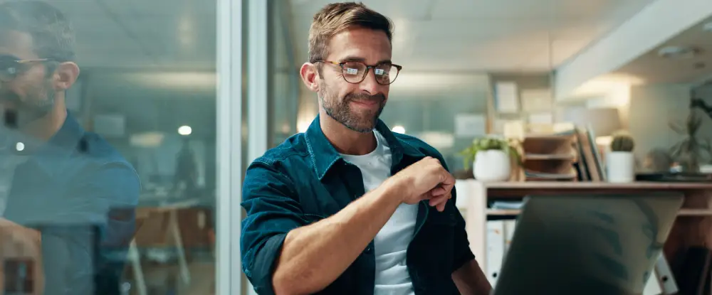 Een man kijkt met een geïnteresseerde glimlach naar zijn laptopscherm, passend bij het ontdekken van nieuwe klantinzichten